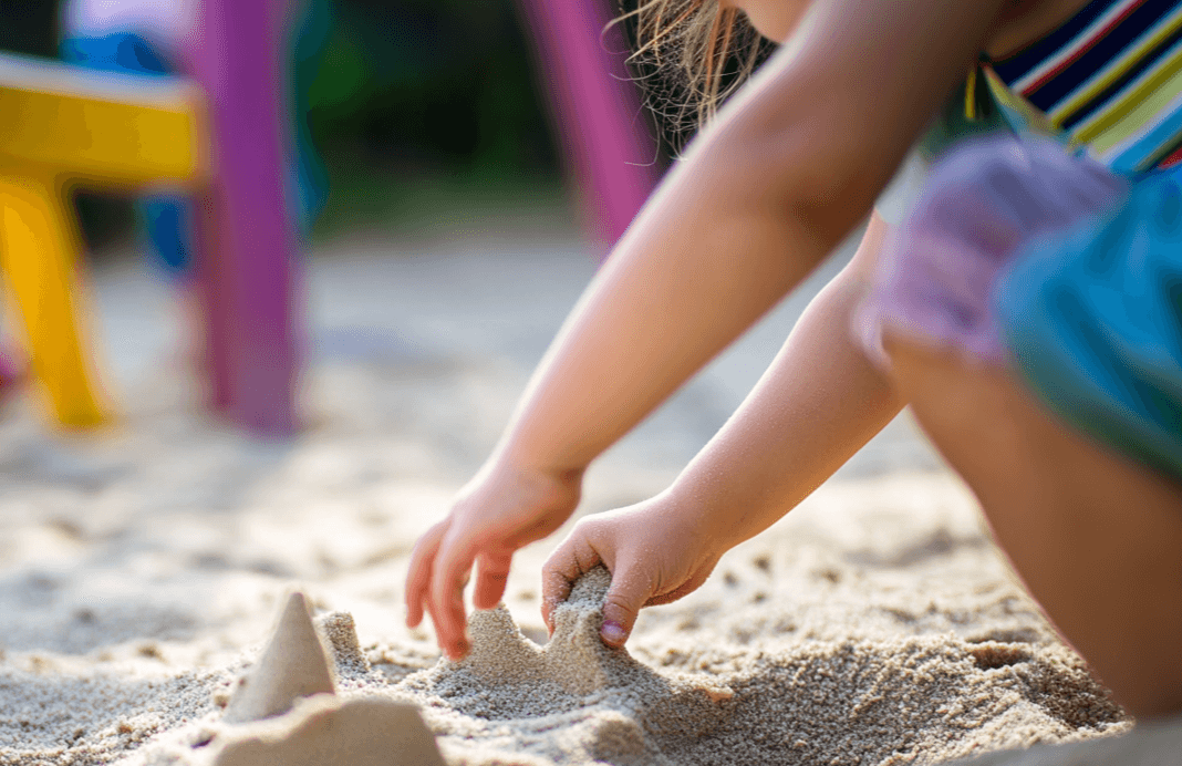 Ein kleines Mädchen spielt mit ihren Händen im Sand und baut eine Sandburg.